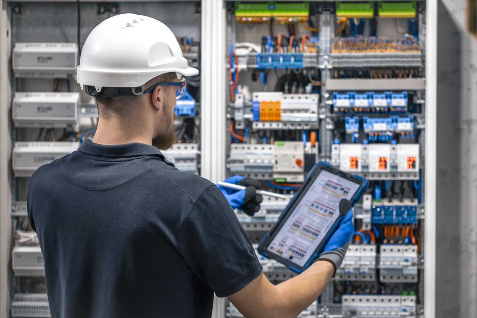 Boletín eléctrico: electricista con casco revisando un cuadro eléctrico con una tableta
