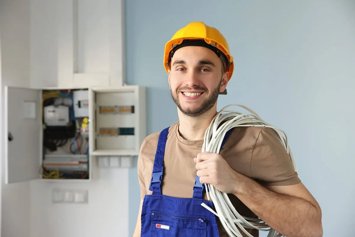 Electricistas en Elche: profesional con casco y un rollo de cable junto a un cuadro de vivienda