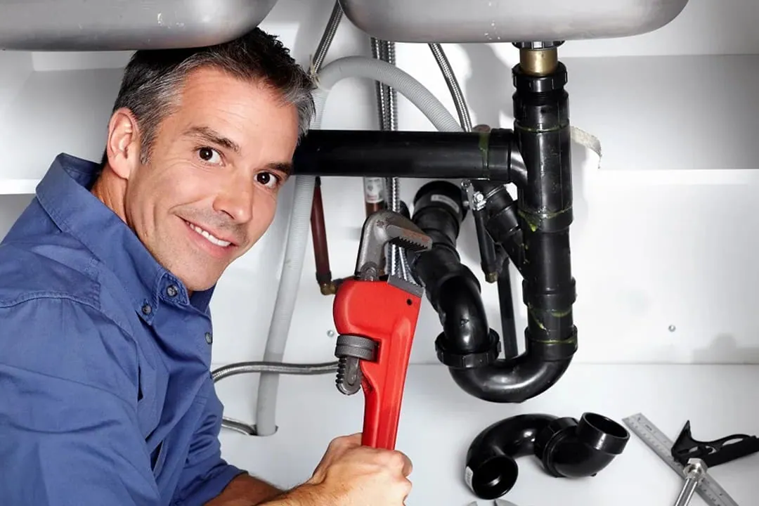 Fontaneros a domicilio: fontanero con llave grifa trabajando bajo un lavabo