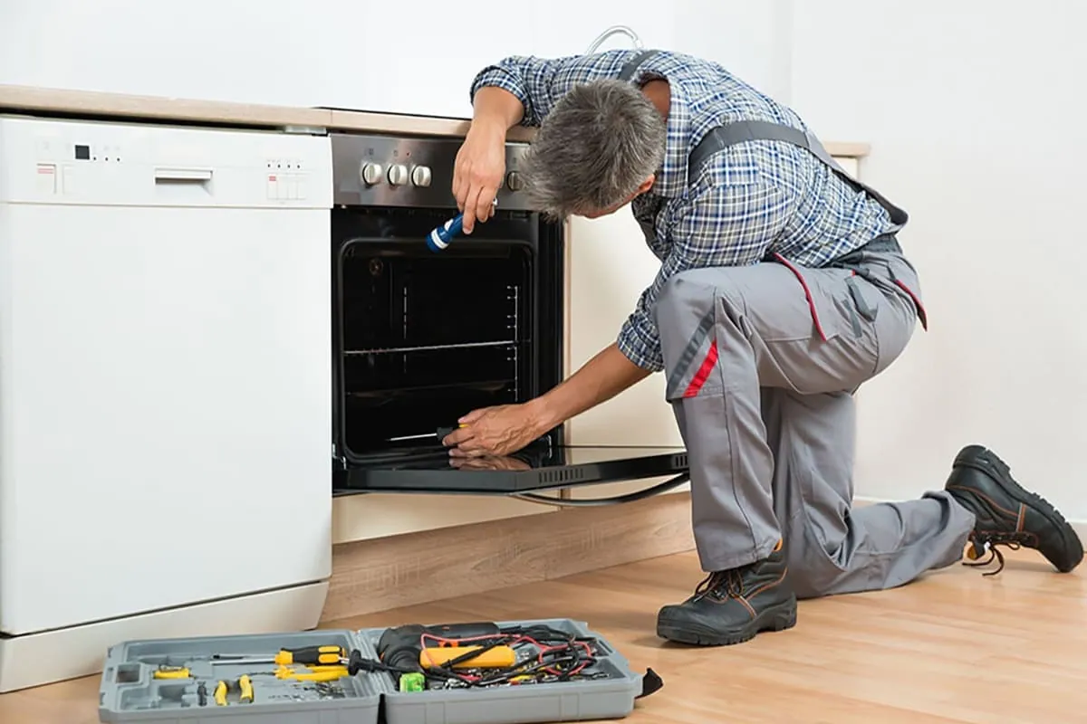Técnico reparando un horno con el aparato fuera del hueco