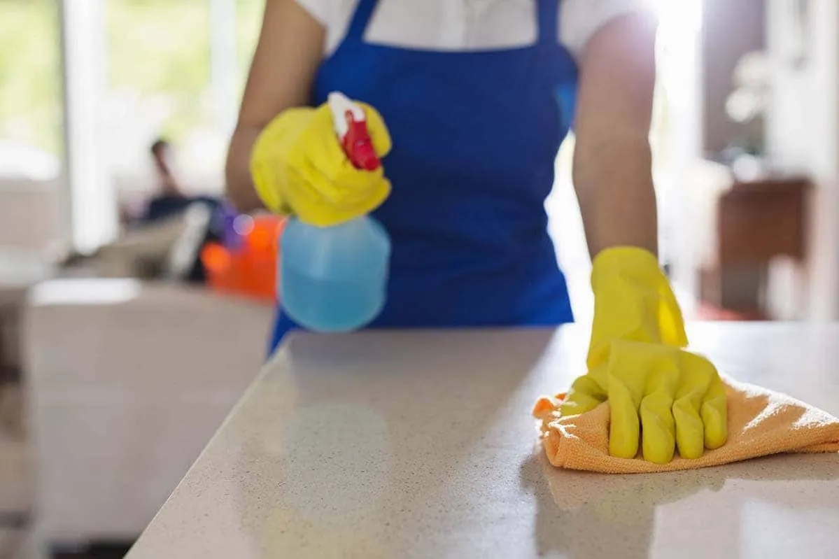 Limpieza de una encimera con pulverizador y bayeta en un servicio de limpieza de cocina