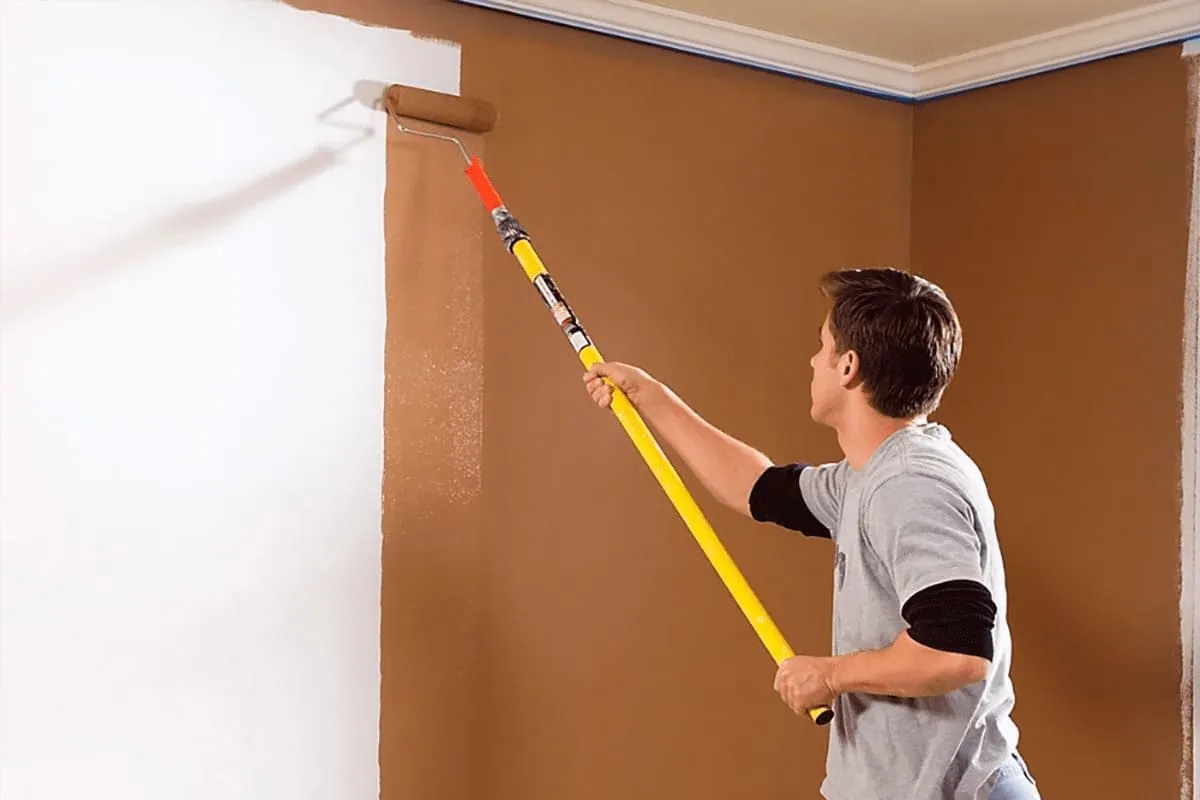 Pintor con rodillo de mango largo en una pared, trabajo habitual de los pintores de pisos