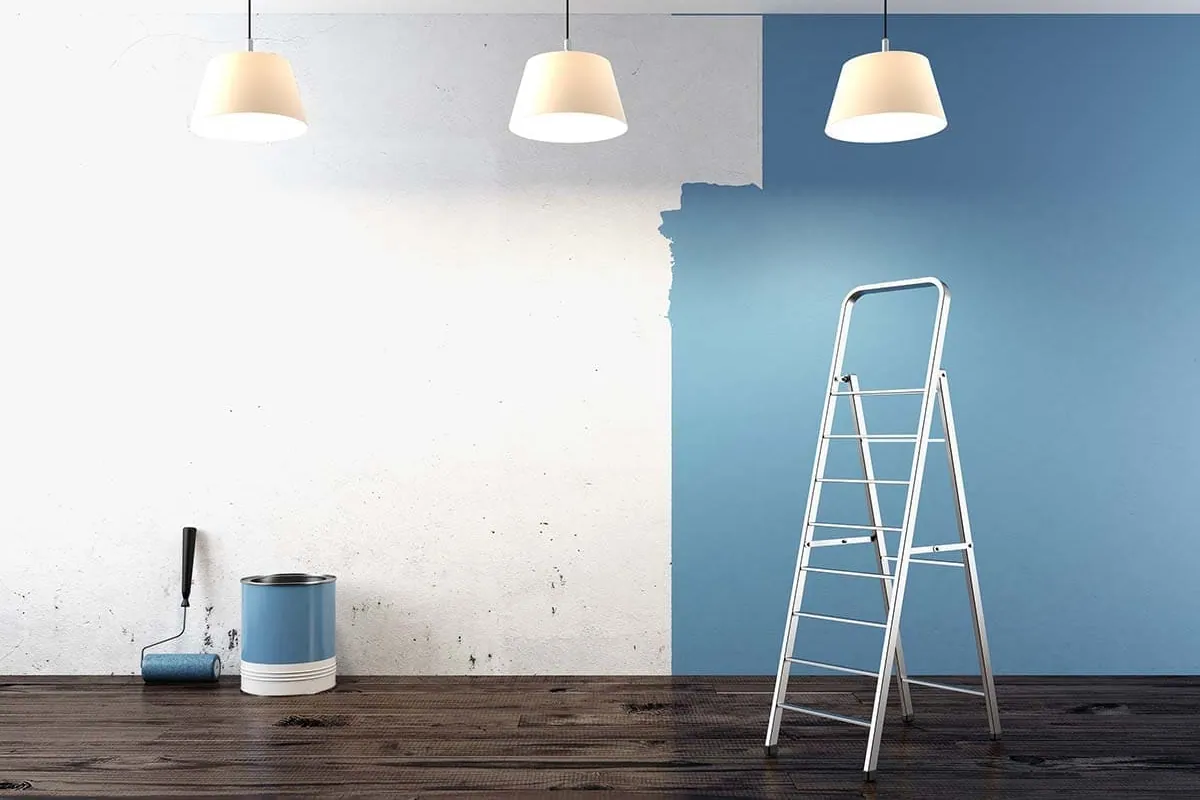 Pintores en Alicante: pared a medio pintar con escalera y cubos de pintura en un piso