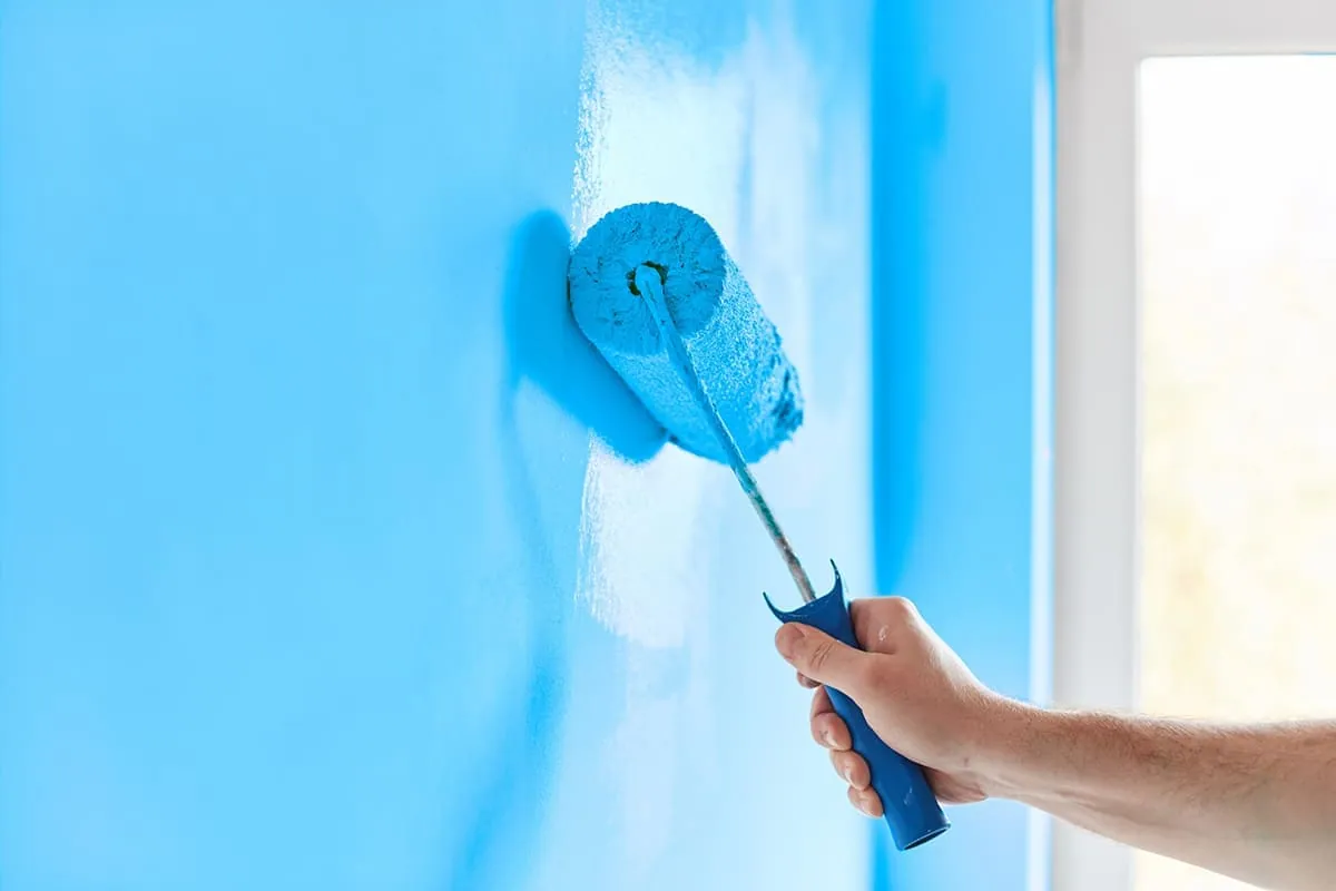 Rodillo aplicando pintura azul en una pared de un local de Elche