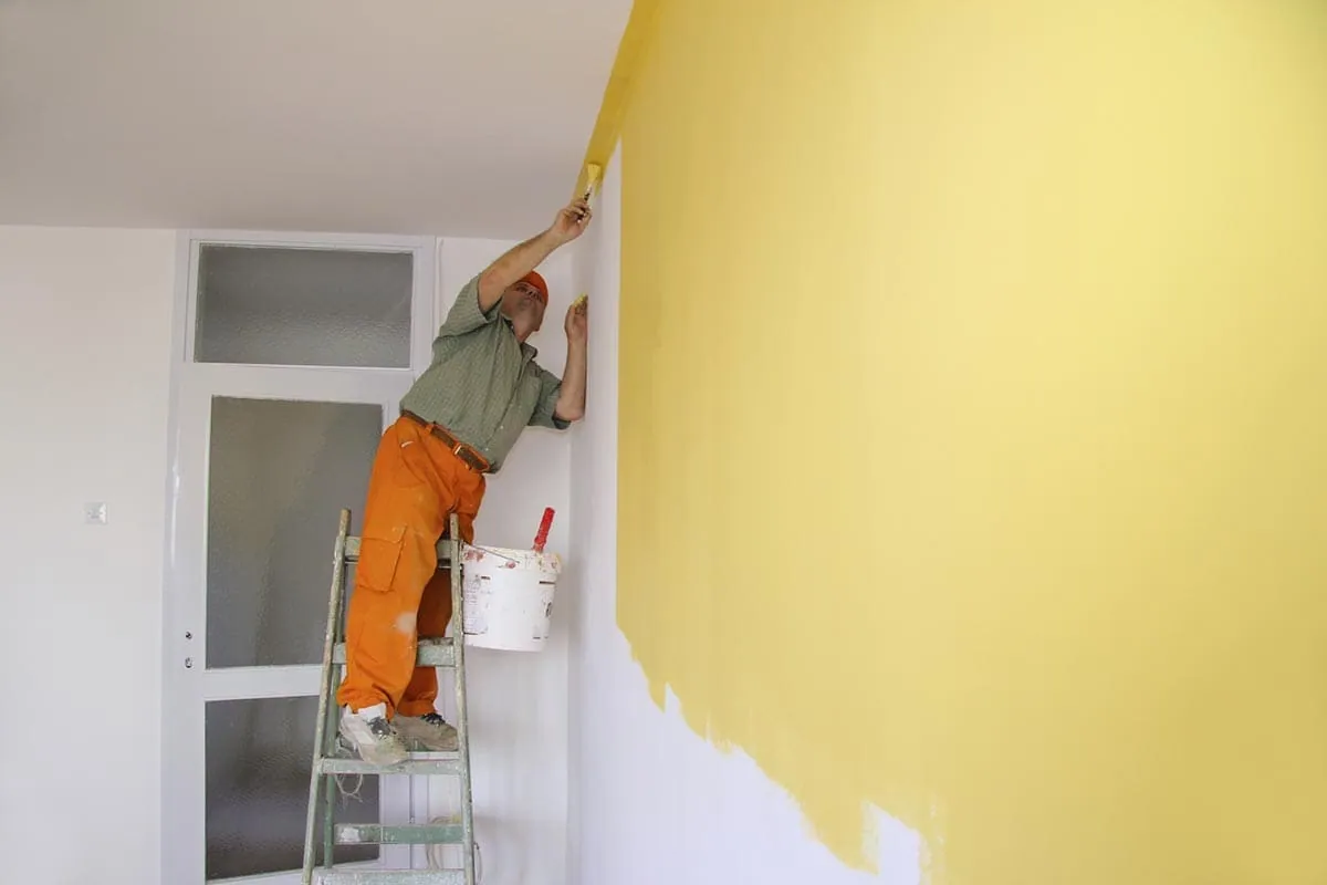 Pintores en Elche: pintor subido a una escalera pintando una pared amarilla