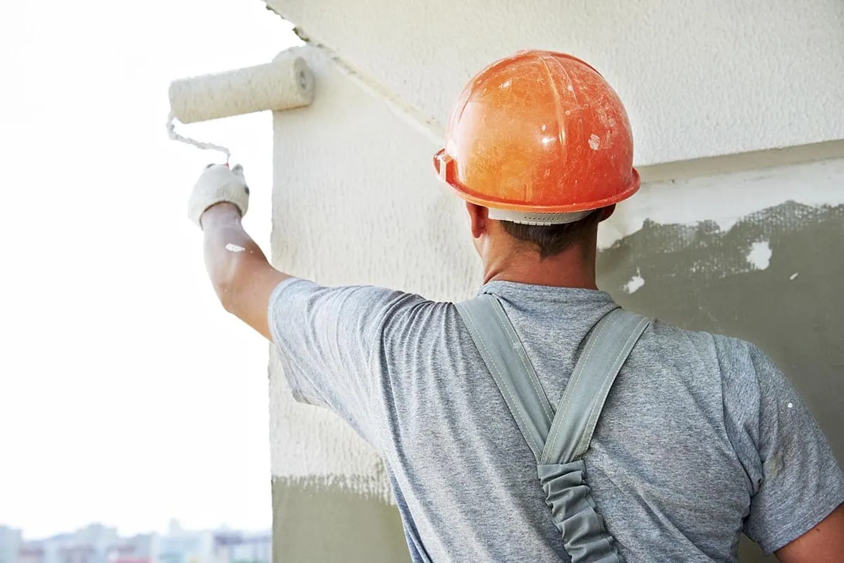 Pintor con casco pintando una fachada, trabajo en altura de pintores en Córdoba