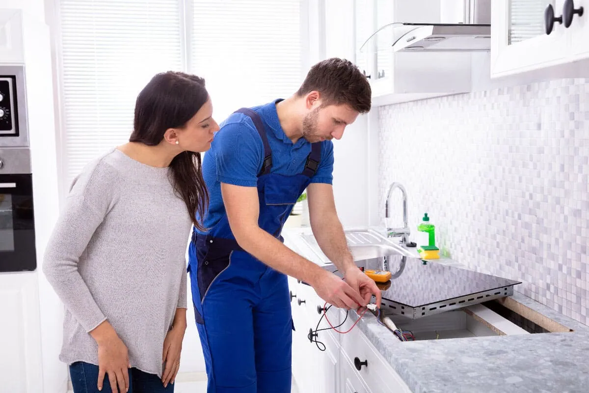 Reparación de placas de inducción: técnico revisando una placa de inducción con la clienta en su cocina